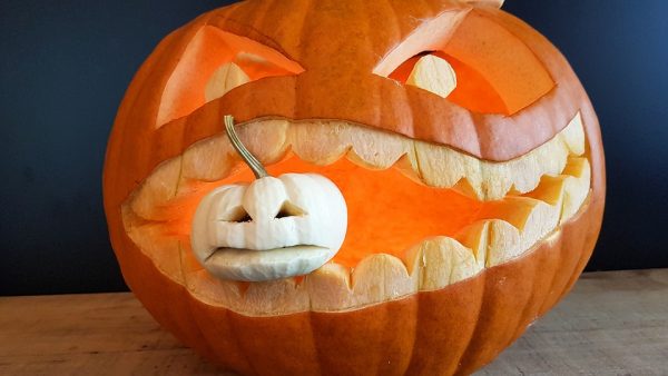 A pumpkin with a smaller pumpkin in its mouth