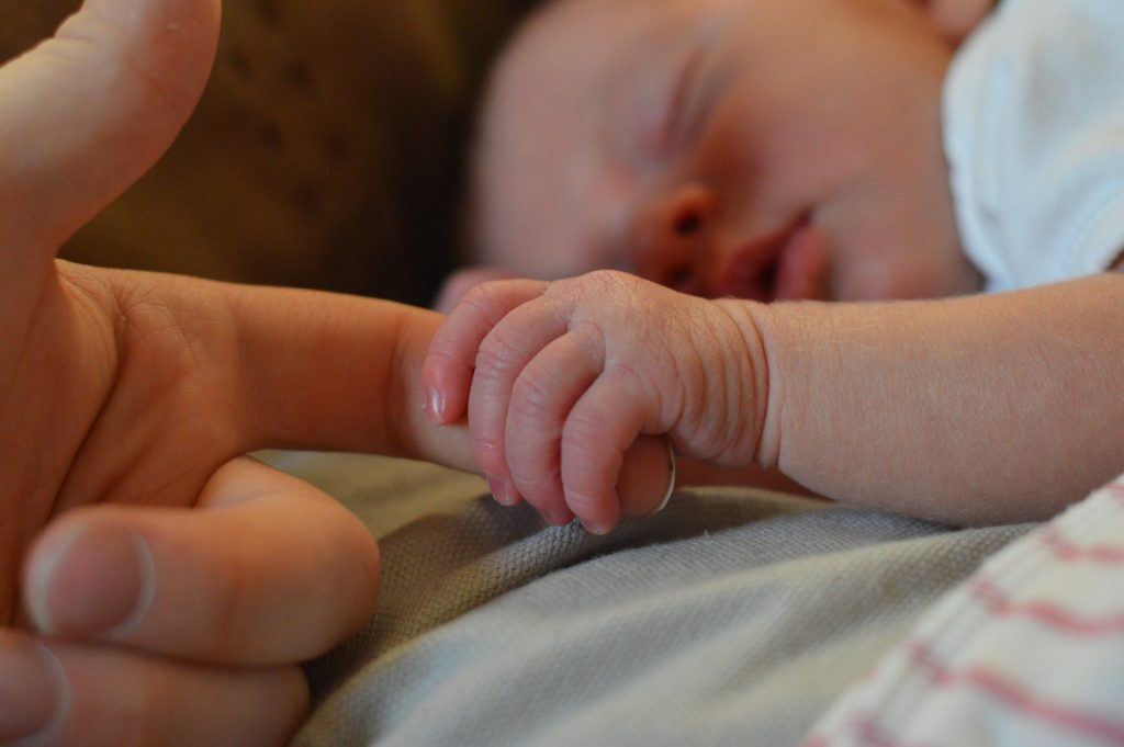 A newborn sleeping and holding his mother's finger