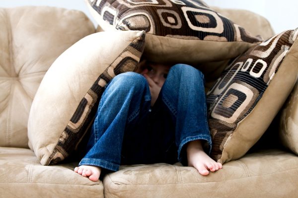 A little girl hiding under pillows