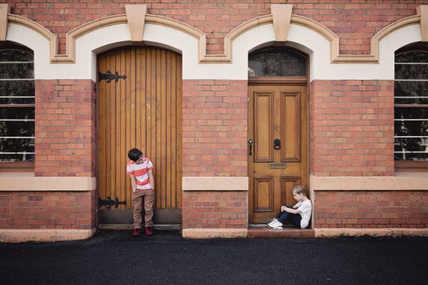 Two boys standing and sitting in front of two doors