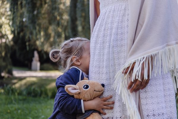 A shy little girl burying her face in her mum's dress