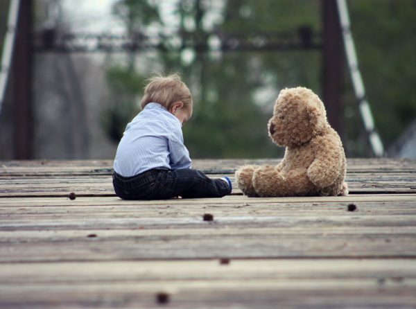 A toddler sitting next to a teddy bear