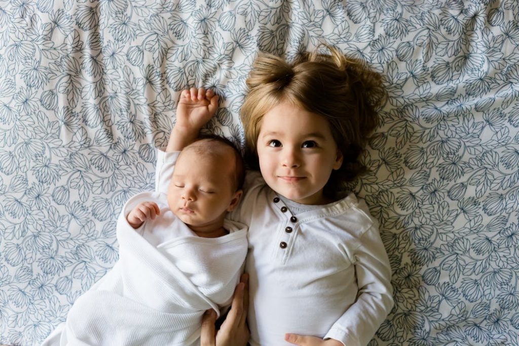 swaddled baby and a young girl lying together