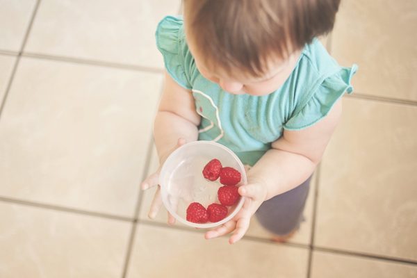 A little girl looking into a bowl with fruit in it