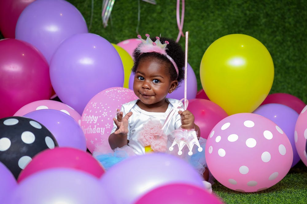 A little girl sitting among birthday balloons