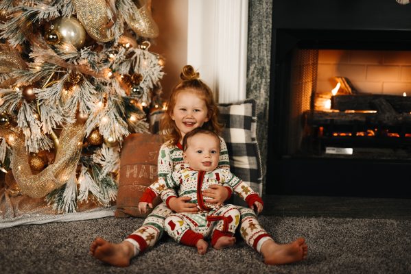 two children posing by a christmas tree to represent how to be happy this christmas