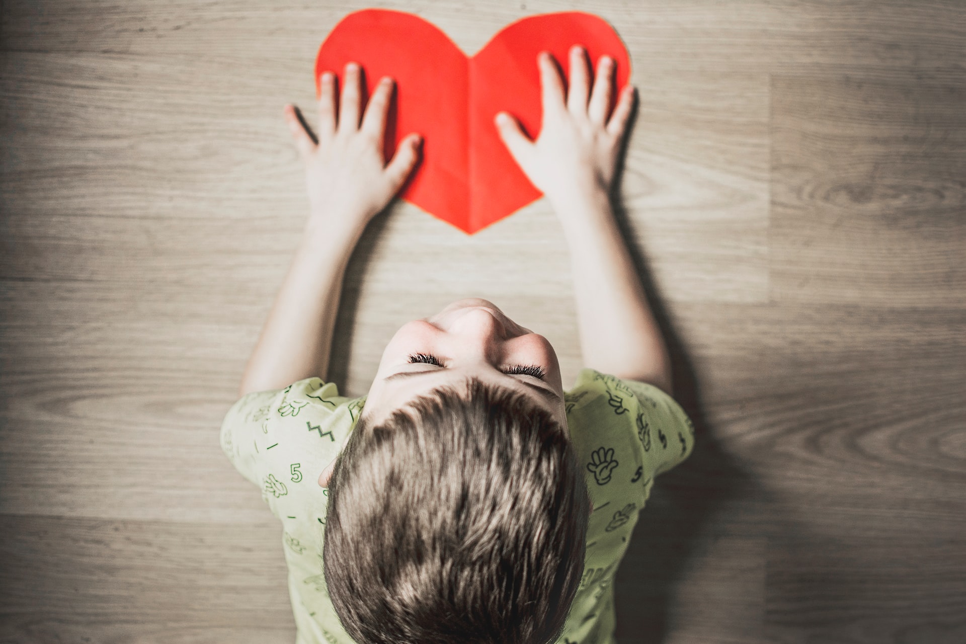 A child lying on their front holding a heart, representing how to teach your child about charity