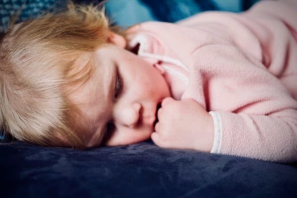 Teething baby lay on the sofa chewing their fingers.