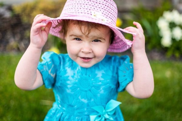 child putting on a pink hat to represent forming habits as part of creating a daily routine for toddlers