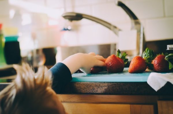 Child grabbing strawberries from the countertop to demonstrate sharing a family meal