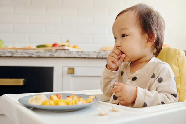 a toddler eating in a highchair to represent how young children can help in the kitchen