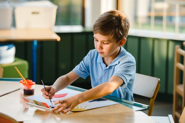 Boy painting in a school uniform to represent starting school