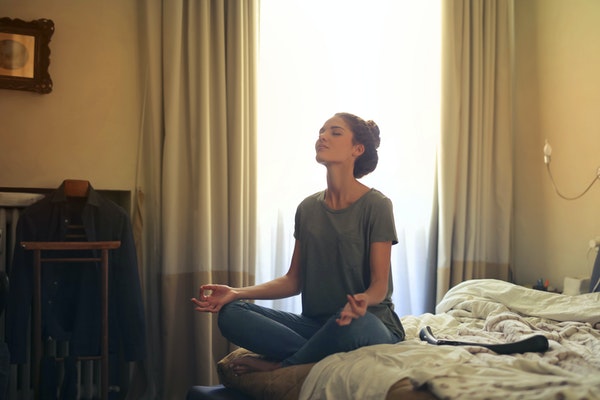 Woman meditating on her bed to represent preparing your child for starting school