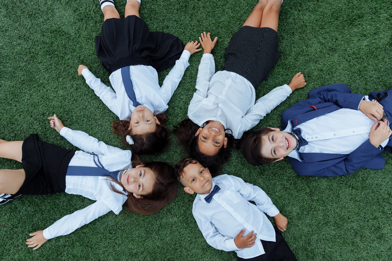 Five children lay on the grass in school uniforms to represent starting school