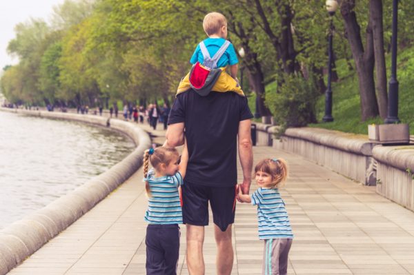 Father holding hands with daughters whilst carrying third child on his shoulders to represent family days out in Wales