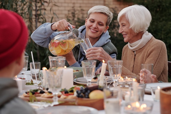 Family dinner party showing a woman pouring water into an older woman's glass to represent how to prioritise self-care as a parent